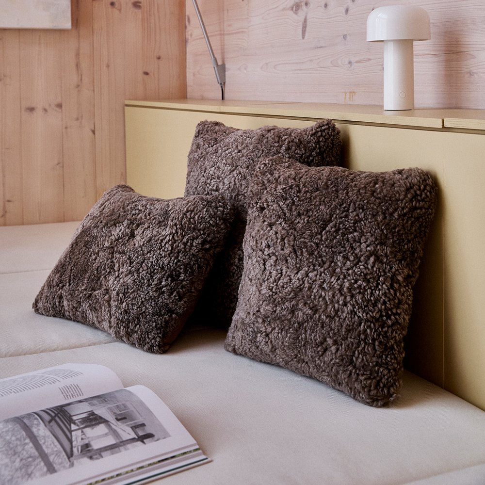 Two brown curly sheepskin cushions on a daybed