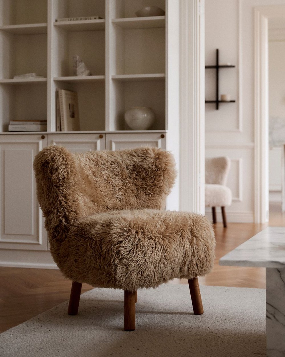Emily lounge chair in honey New Zealand long hair on dark wood legs beside white shelving