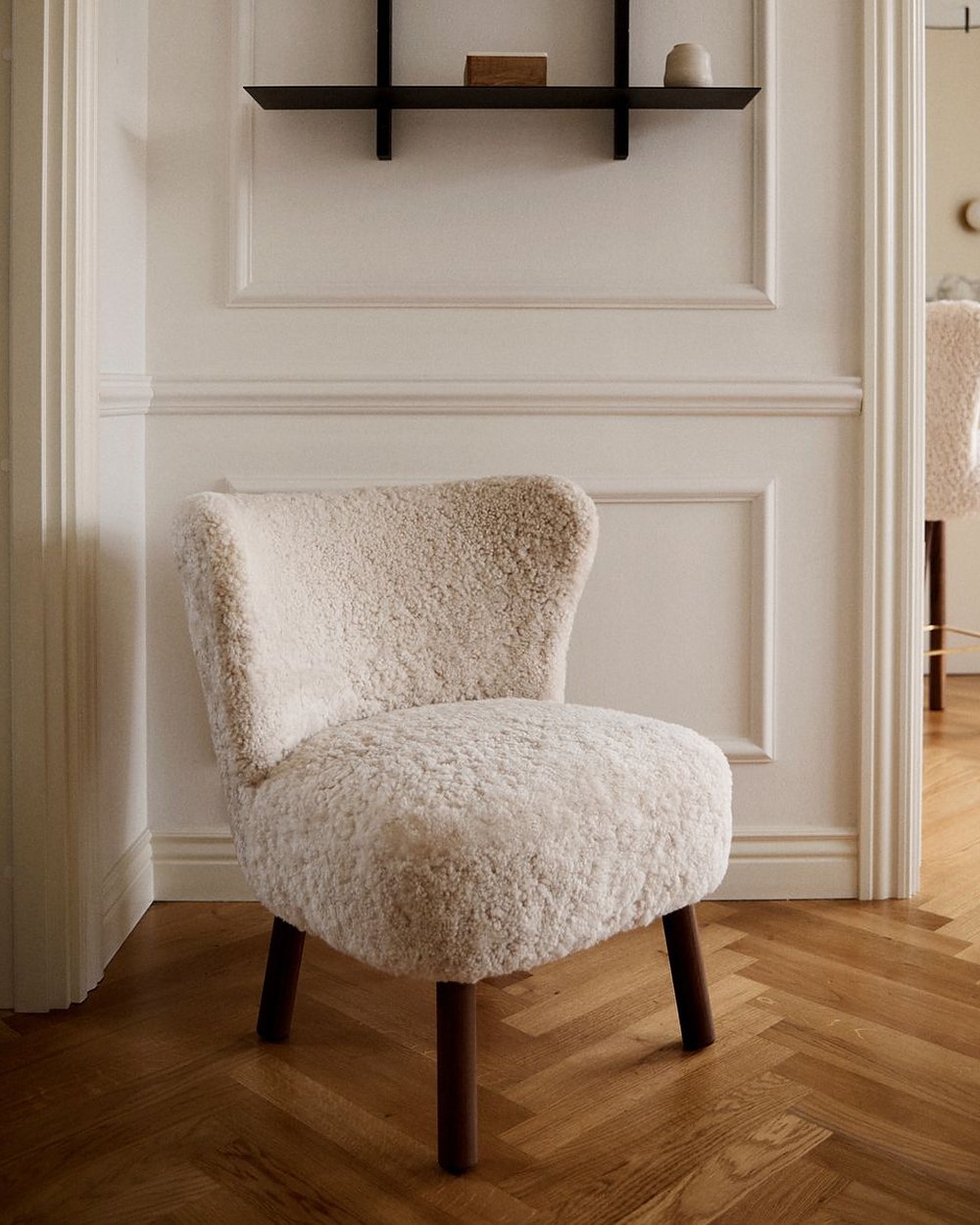 Emily lounge chair in pearl short hair on walnut legs by a paneled wall