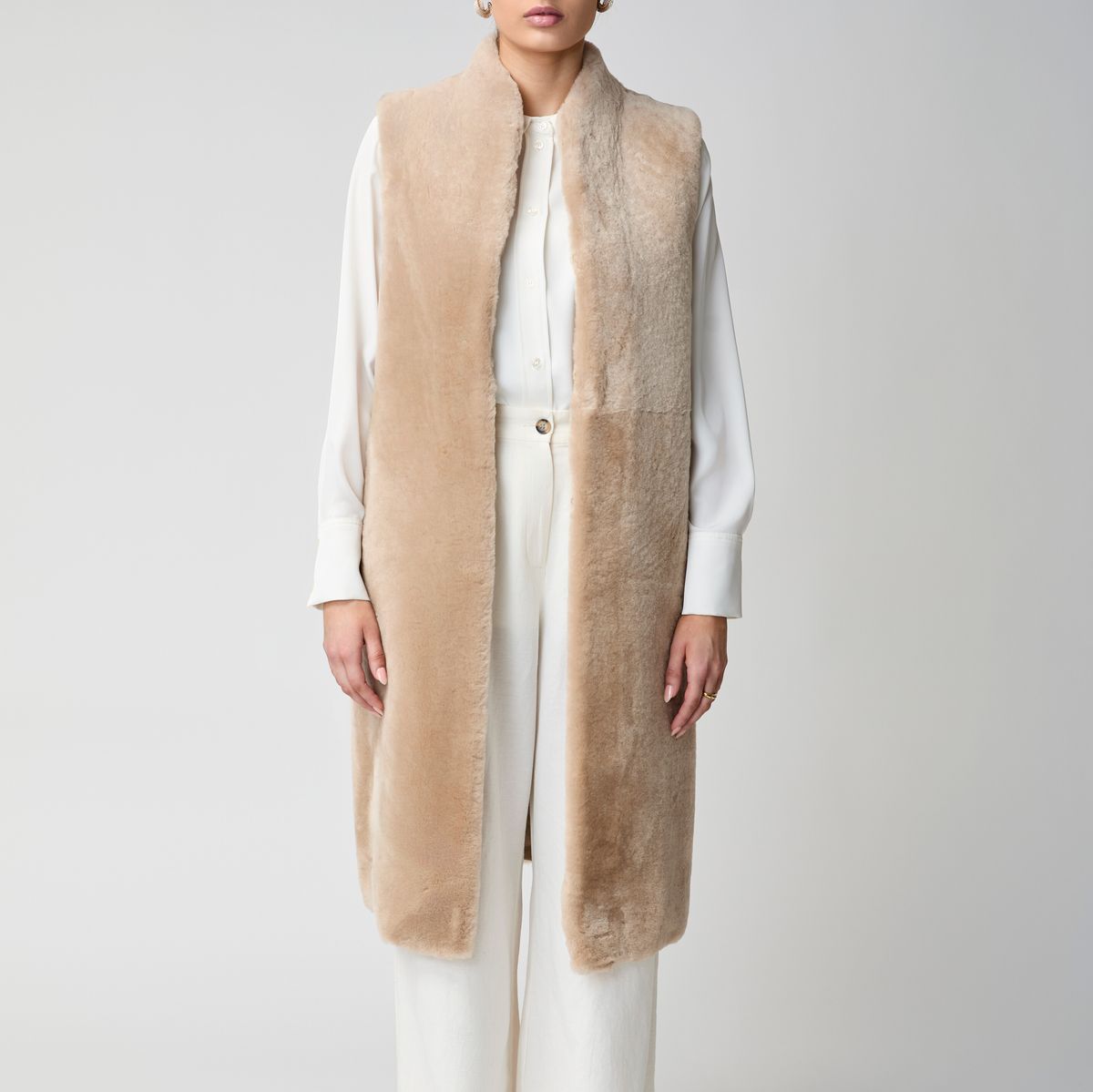Woman wearing a long camel shearling vest over a white shirt