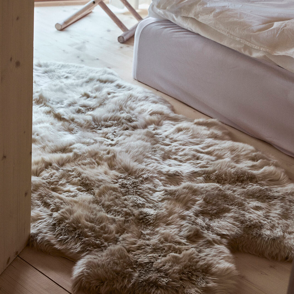 Large multi pelt sheepskin rug beside a bed