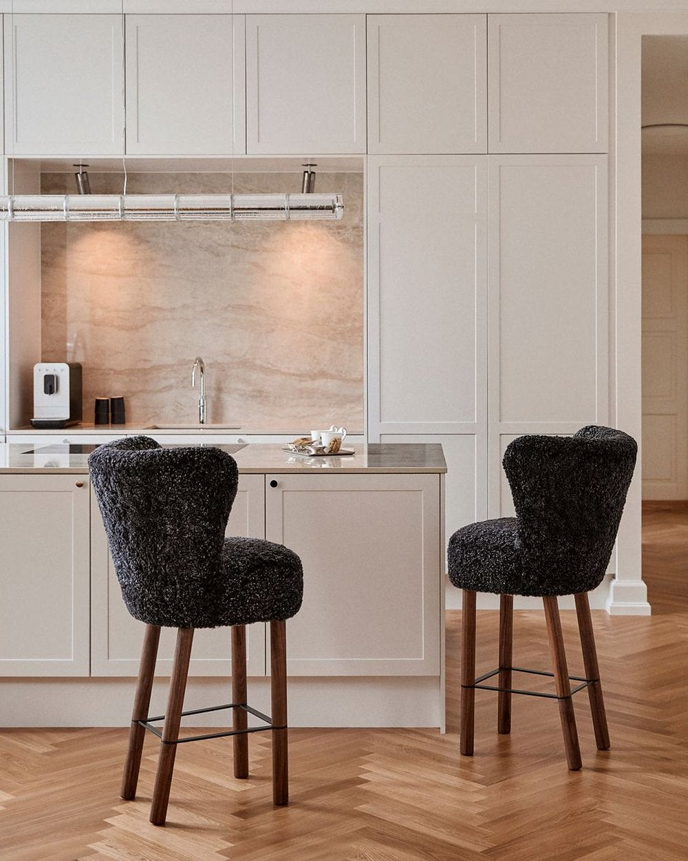 Two Emilia bar stools in dark gray short hair on walnut legs with black steel foot rails at a kitchen island