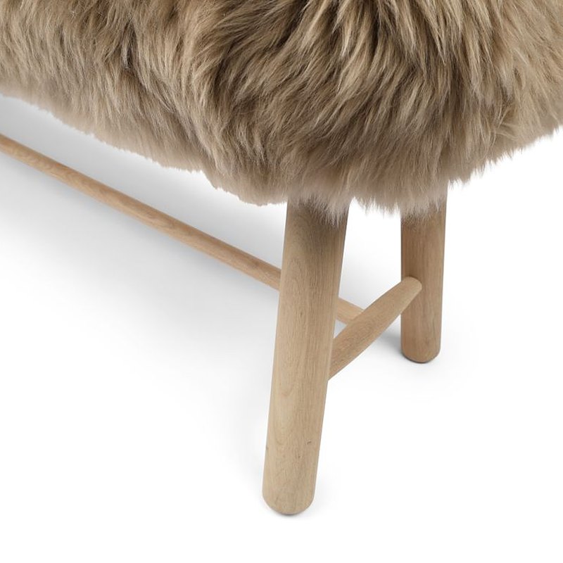 Detail of an oak leg and stretcher in a light finish under taupe long hair on a bench