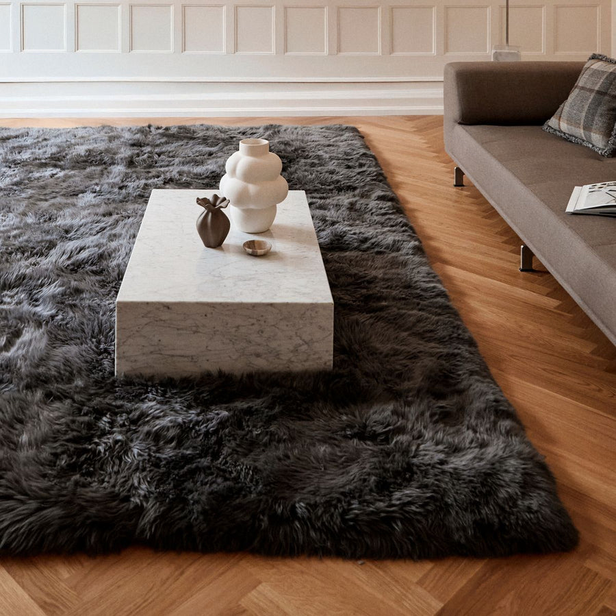 Dark gray long hair rug under a stone coffee table on a herringbone floor