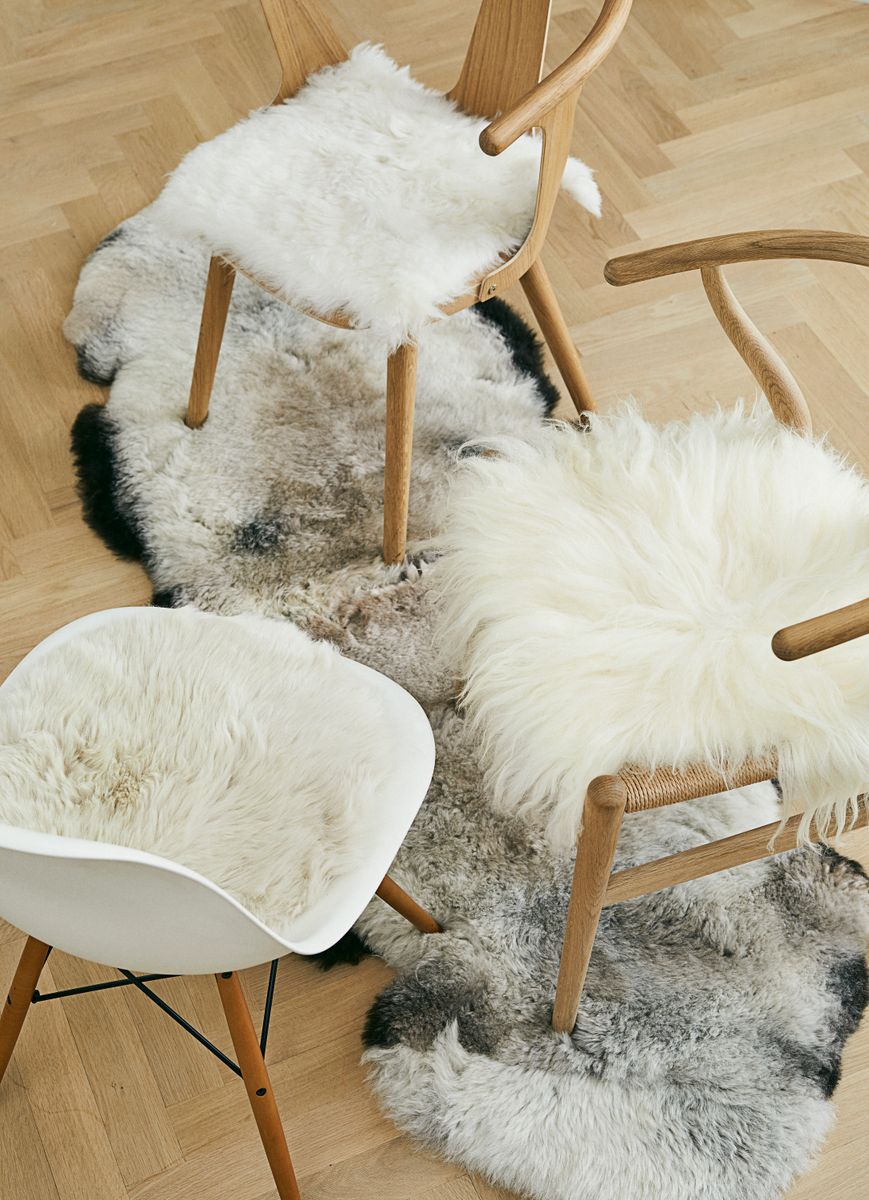 Sheepskin seat covers on three dining chairs, standing on a long gray sheepskin rug on a herringbone floor