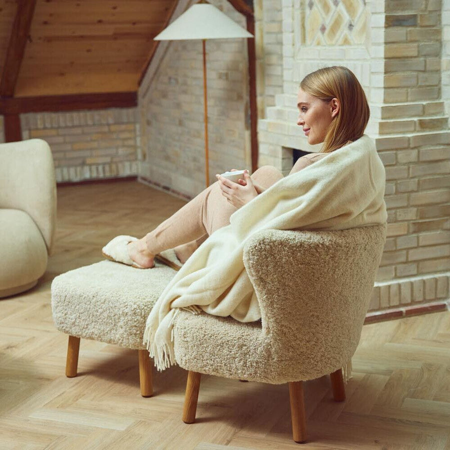 Woman with a mug in a curly sheepskin lounge chair with a matching foot rest on wooden legs